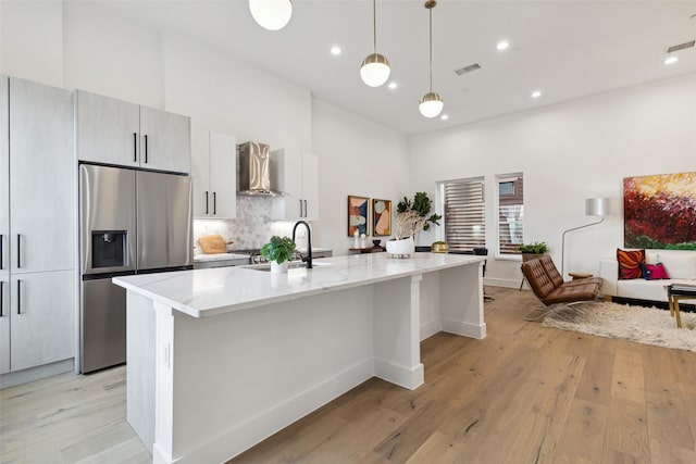 kitchen with a spacious island, a sink, visible vents, wall chimney exhaust hood, and stainless steel fridge