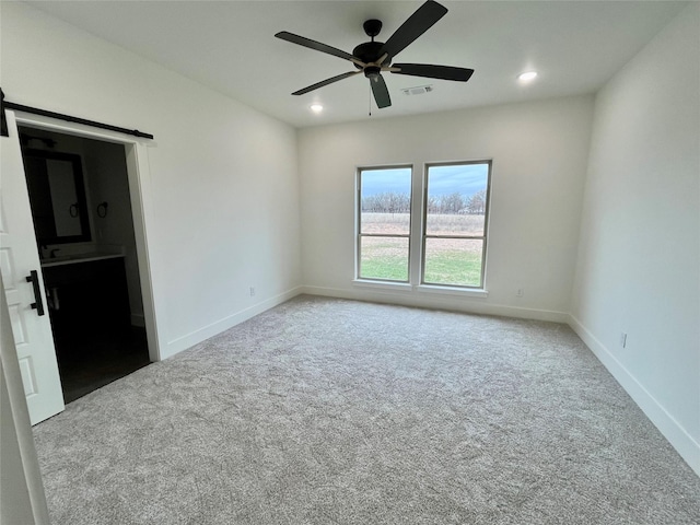 carpeted spare room featuring a barn door and ceiling fan