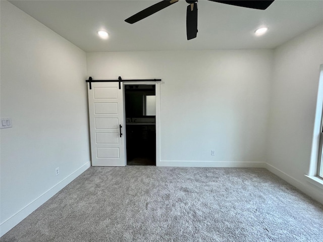 unfurnished bedroom with a barn door, ceiling fan, and carpet