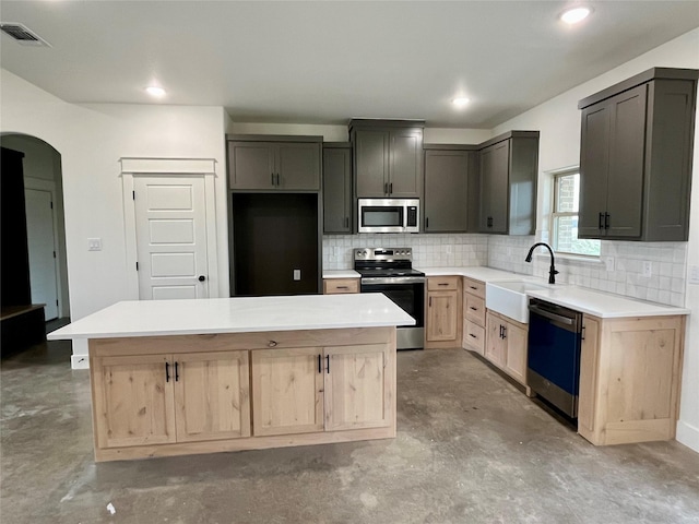 kitchen featuring a kitchen island, gray cabinetry, concrete floors, stainless steel appliances, and light brown cabinets