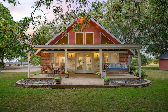 back of property at dusk featuring stone siding, french doors, brick siding, and a lawn