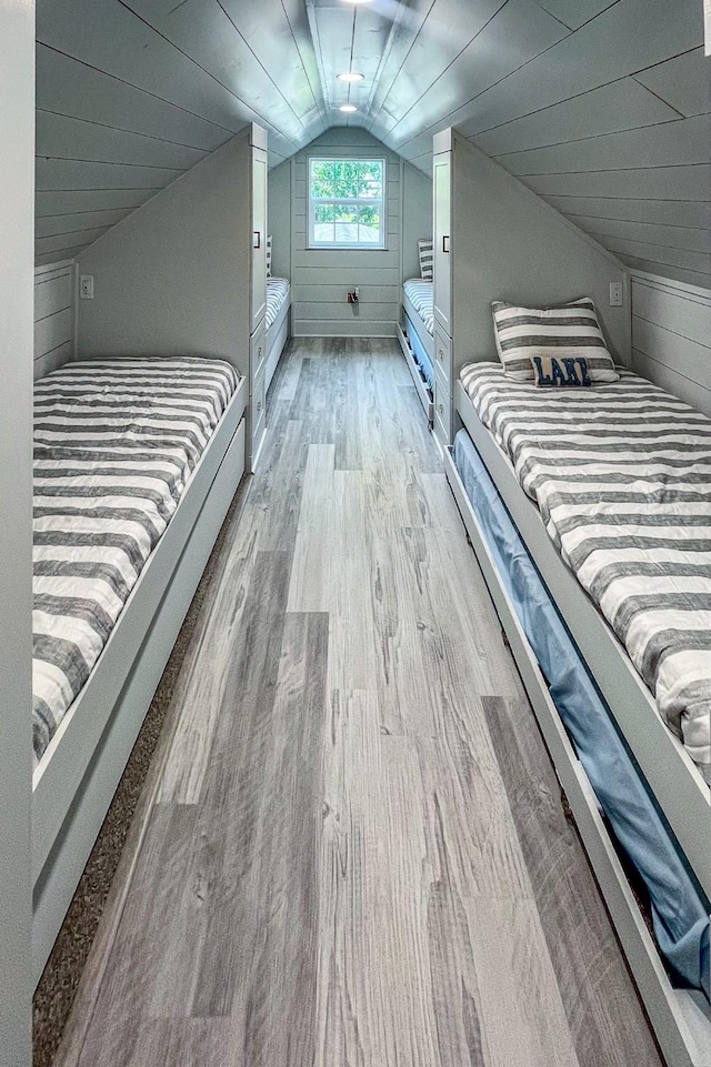 unfurnished bedroom featuring lofted ceiling, wooden walls, and wood finished floors