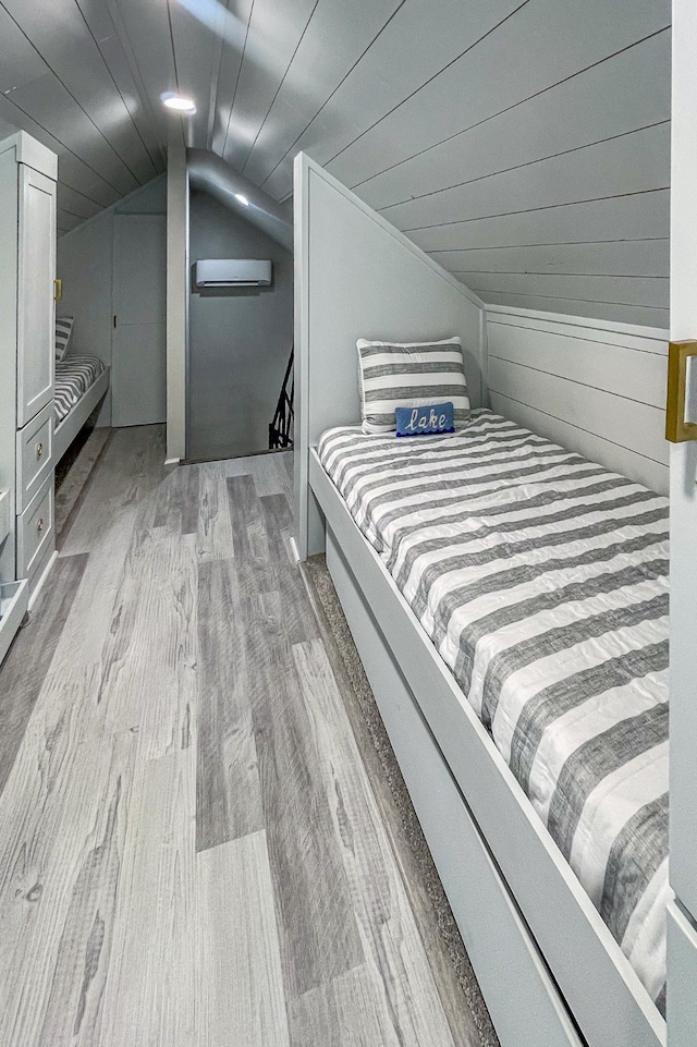 bedroom featuring a wall unit AC, wood walls, light hardwood / wood-style floors, and vaulted ceiling