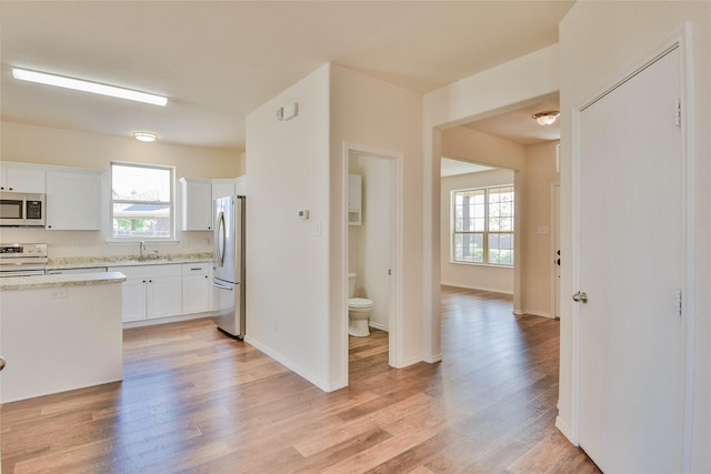 kitchen with white cabinets, sink, light stone countertops, appliances with stainless steel finishes, and light hardwood / wood-style floors