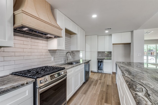 kitchen with custom range hood, stainless steel appliances, sink, and white cabinets