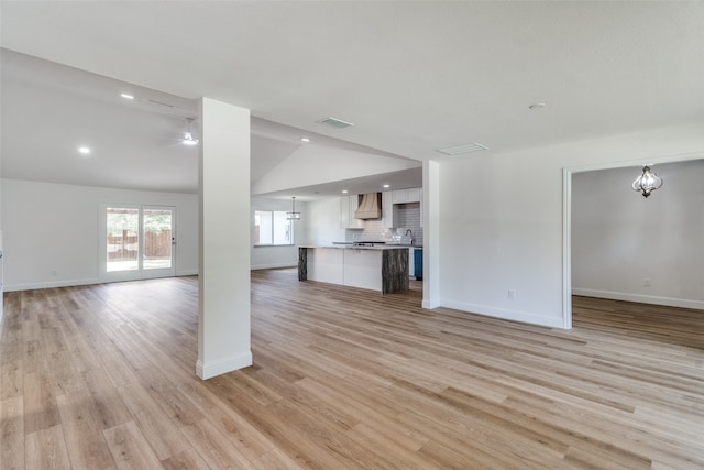 unfurnished living room featuring lofted ceiling, light hardwood / wood-style flooring, and ceiling fan with notable chandelier