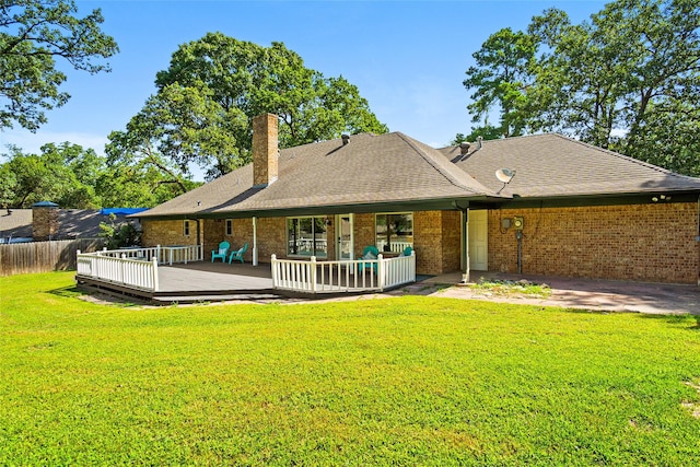 rear view of house with a lawn, fence, a wooden deck, brick siding, and a chimney