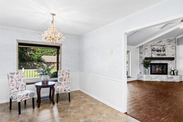 living area featuring crown molding, vaulted ceiling, a brick fireplace, ceiling fan with notable chandelier, and wood-type flooring