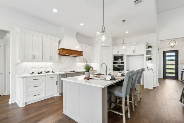 kitchen with dark hardwood / wood-style flooring, premium range hood, an island with sink, sink, and white cabinetry