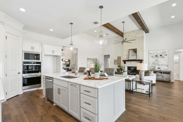 kitchen with white cabinets, light stone countertops, a stone fireplace, ceiling fan, and a center island with sink