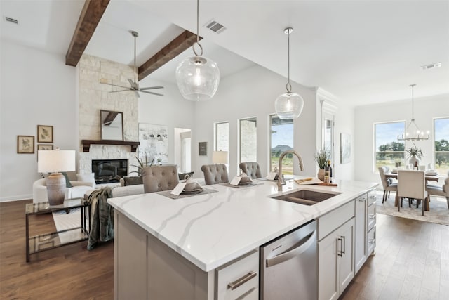 kitchen with ceiling fan with notable chandelier, a fireplace, an island with sink, stainless steel dishwasher, and sink