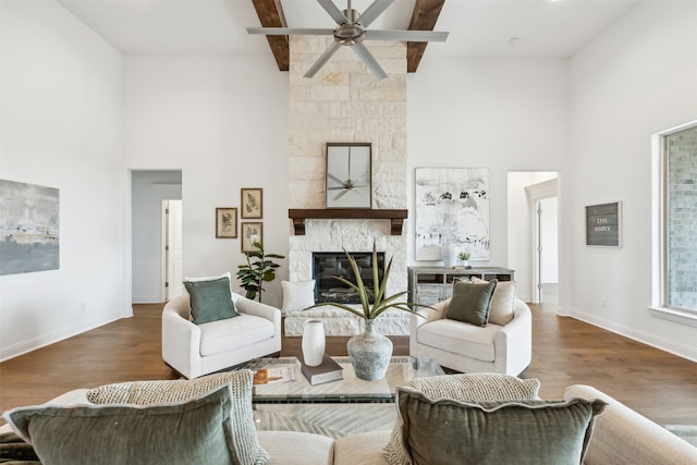 living room with beamed ceiling, a fireplace, wood-type flooring, ceiling fan, and a towering ceiling