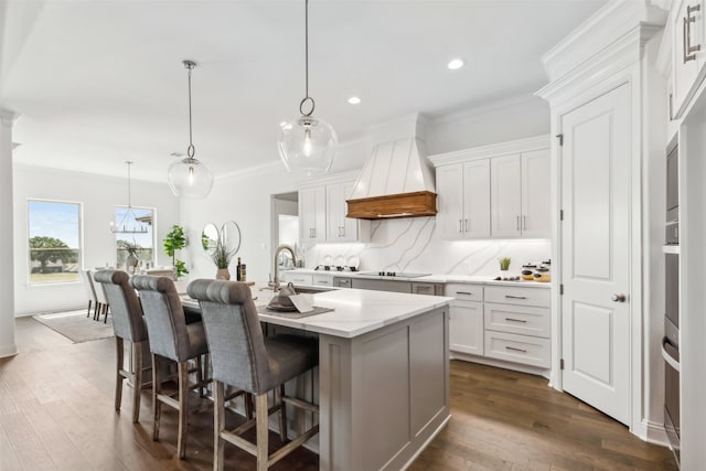 kitchen featuring an island with sink, premium range hood, and white cabinets