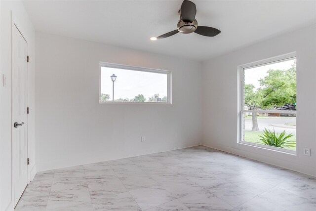 empty room featuring healthy amount of natural light, light marble finish floors, and a ceiling fan