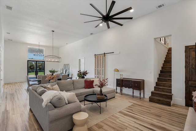 living room featuring ceiling fan with notable chandelier, light wood-type flooring, and a barn door