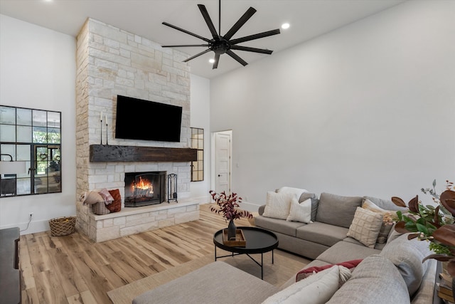 living room featuring light hardwood / wood-style floors, a high ceiling, a fireplace, and ceiling fan