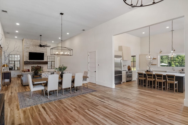 dining room with ceiling fan, a high ceiling, light wood-type flooring, and a fireplace