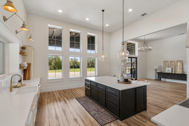 kitchen featuring hanging light fixtures, a kitchen island, a towering ceiling, light hardwood / wood-style floors, and sink