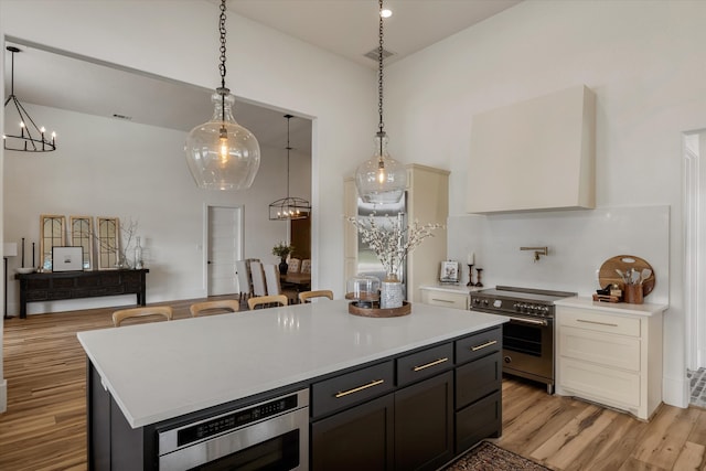 kitchen with appliances with stainless steel finishes, a center island, hanging light fixtures, white cabinets, and light hardwood / wood-style flooring