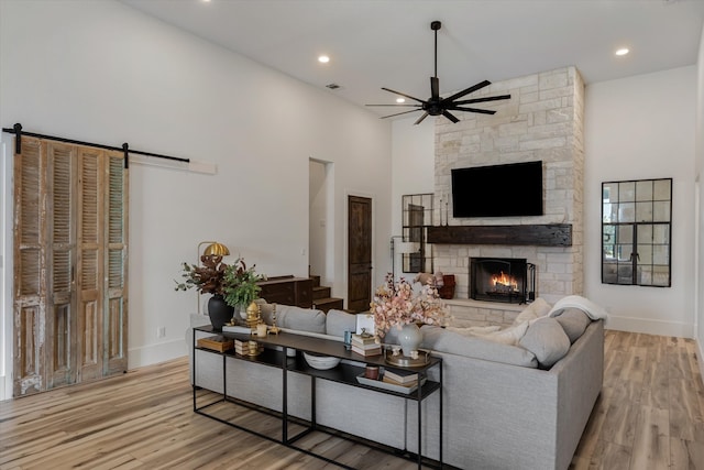 living room with a barn door, a fireplace, a towering ceiling, and light hardwood / wood-style floors