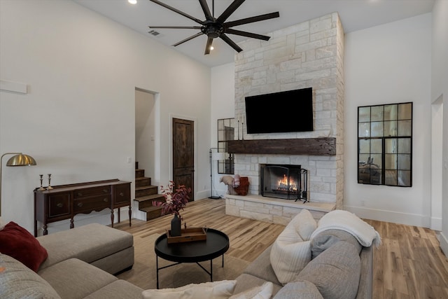 living room with a fireplace, a high ceiling, light wood-type flooring, and ceiling fan