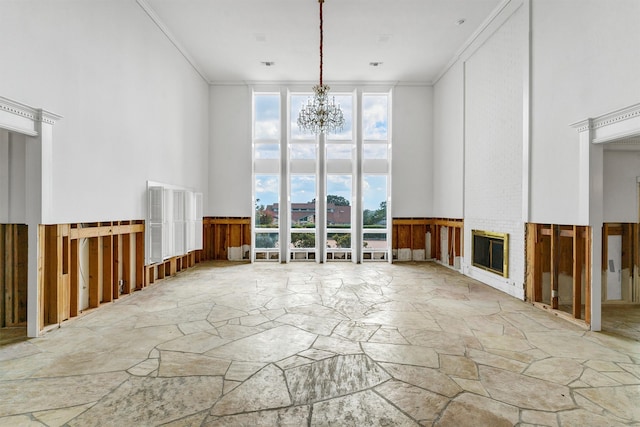 spare room with crown molding, a high ceiling, an inviting chandelier, and a brick fireplace