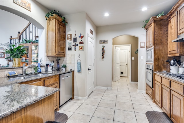 kitchen featuring appliances with stainless steel finishes, decorative backsplash, light stone counters, and light tile patterned floors