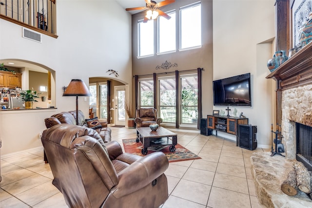 tiled living room featuring ceiling fan, a high ceiling, plenty of natural light, and a fireplace