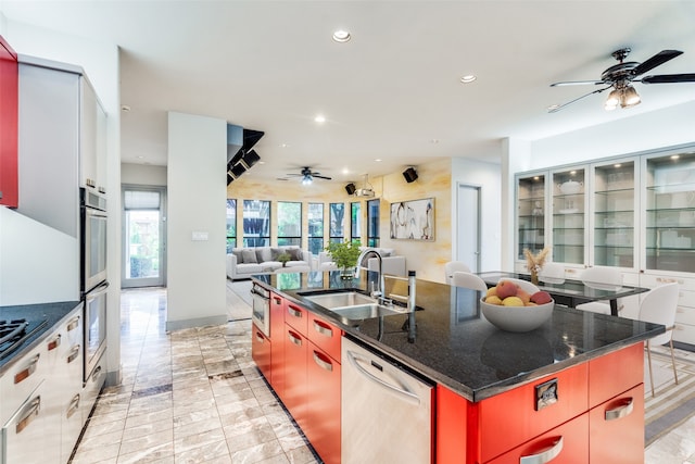 kitchen featuring dark stone countertops, stainless steel appliances, a large island with sink, ceiling fan, and sink