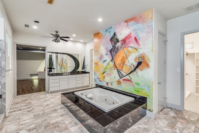 bathroom featuring ceiling fan, a relaxing tiled tub, and vanity