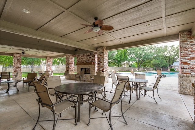 view of patio / terrace with an outdoor brick fireplace, ceiling fan, and a fenced in pool