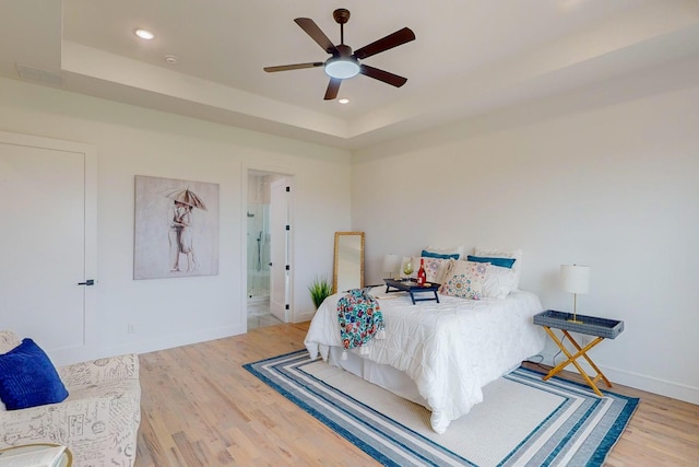 bedroom featuring connected bathroom, a tray ceiling, ceiling fan, and hardwood / wood-style flooring