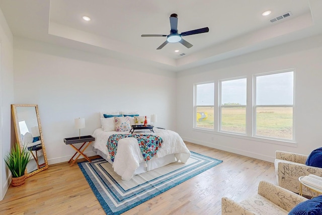 bedroom featuring light hardwood / wood-style flooring, ceiling fan, and a raised ceiling