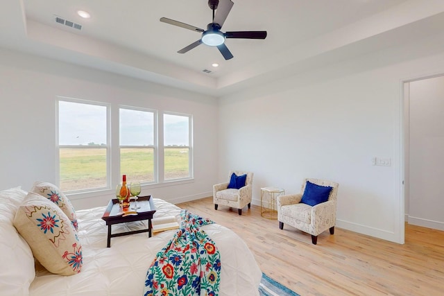 living area with ceiling fan, a tray ceiling, and hardwood / wood-style floors