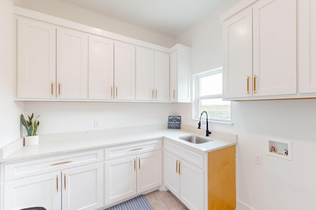 kitchen with white cabinetry, light stone counters, light tile patterned floors, and sink