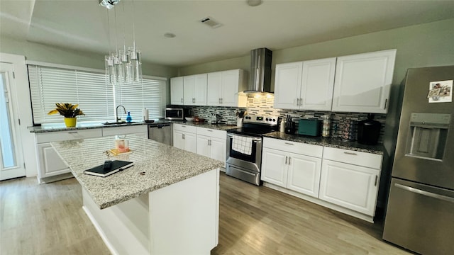 kitchen with light wood-type flooring, stainless steel appliances, white cabinetry, wall chimney exhaust hood, and a kitchen island