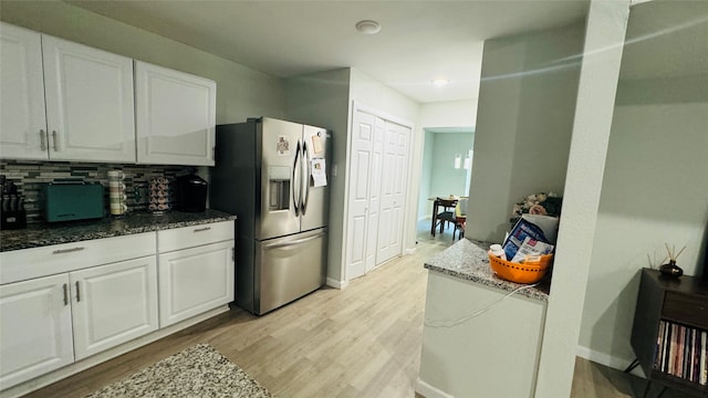 kitchen with backsplash, dark stone countertops, light wood-type flooring, white cabinetry, and stainless steel refrigerator with ice dispenser