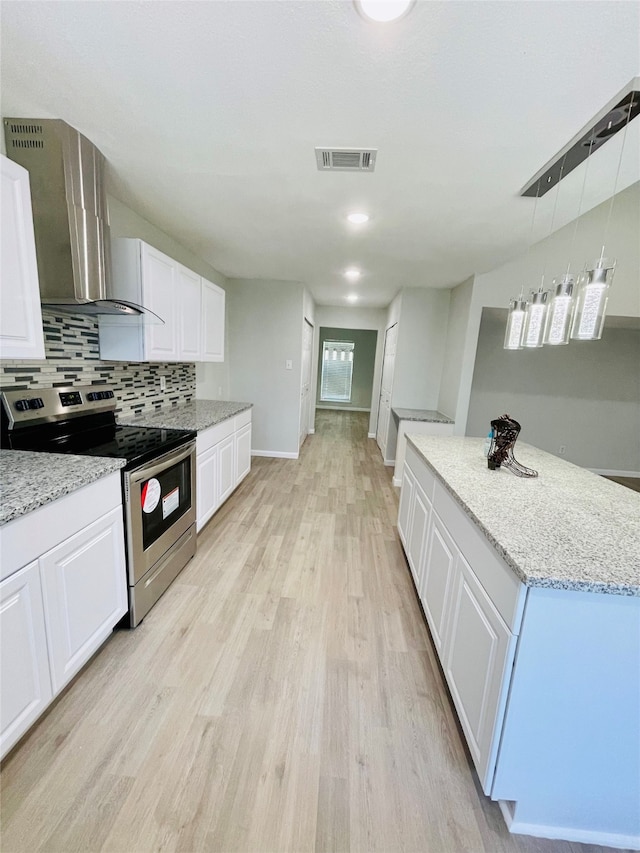 kitchen with wall chimney range hood, stainless steel electric range, light stone counters, and light hardwood / wood-style floors