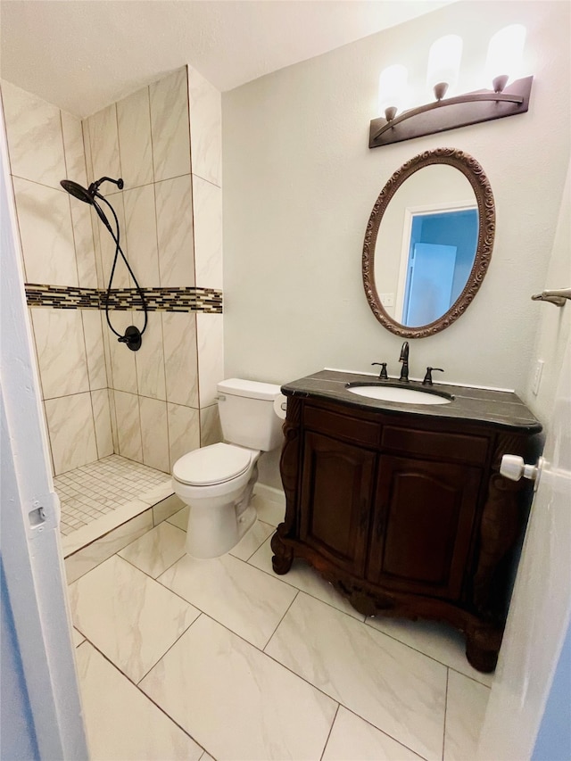 bathroom featuring tile patterned floors, toilet, a tile shower, and vanity