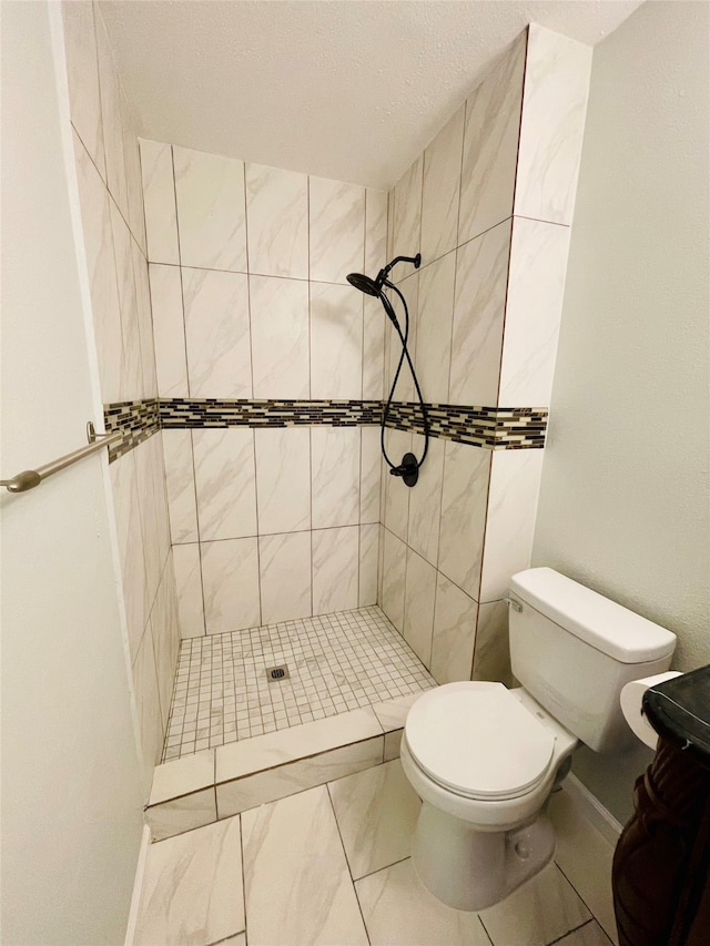 bathroom featuring tile patterned flooring, toilet, and a tile shower