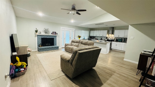 living room featuring vaulted ceiling, light hardwood / wood-style flooring, a brick fireplace, and ceiling fan