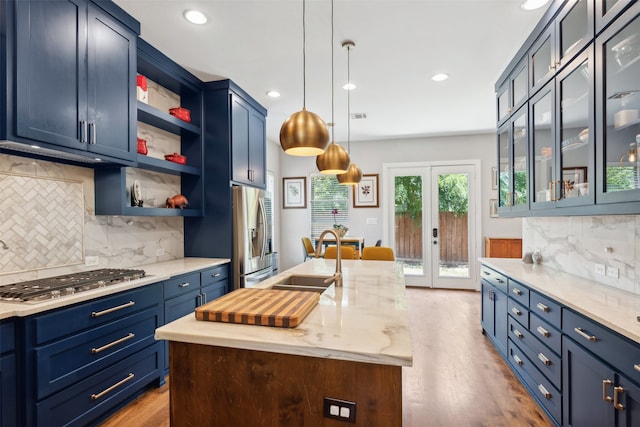 kitchen with light stone countertops, an island with sink, french doors, blue cabinets, and appliances with stainless steel finishes