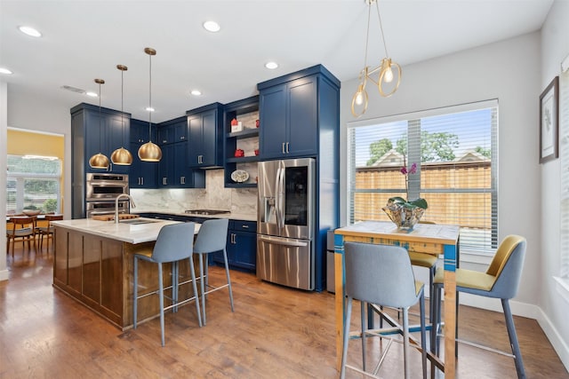 kitchen featuring wood finished floors, appliances with stainless steel finishes, blue cabinetry, decorative backsplash, and open shelves