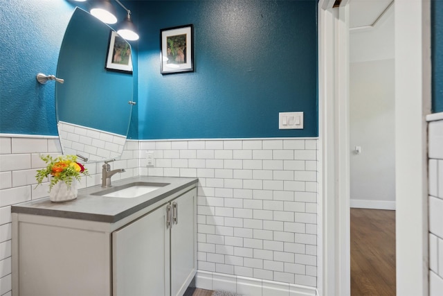 bathroom featuring a textured wall, a wainscoted wall, wood finished floors, vanity, and tile walls