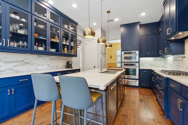 kitchen with decorative light fixtures, a center island with sink, tasteful backsplash, dark hardwood / wood-style flooring, and blue cabinets