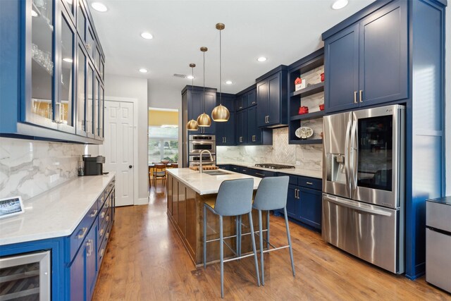 kitchen with appliances with stainless steel finishes, hanging light fixtures, light stone countertops, sink, and backsplash