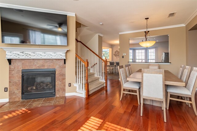 dining space with crown molding, hardwood / wood-style flooring, and a tile fireplace