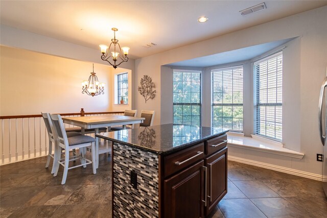 kitchen featuring dark stone counters, dark brown cabinets, a kitchen island, dark tile patterned floors, and an inviting chandelier