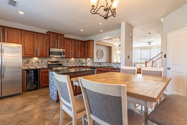 kitchen with decorative light fixtures, ceiling fan with notable chandelier, stainless steel appliances, beverage cooler, and tasteful backsplash