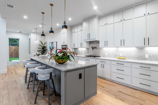 kitchen with a large island with sink, appliances with stainless steel finishes, light hardwood / wood-style floors, white cabinets, and a breakfast bar area